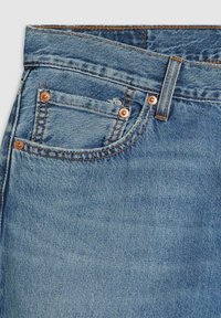 Los jeans de mezclilla en un tono azul claro presentan una cintura plana, herrajes de cobre y un pequeño bolsillo delantero con detalles de costura clásicos.