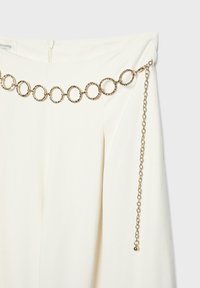 Jupe blanche avec une ceinture chaîne dorée décorative composée de maillons ronds texturés et d'une chaîne pendante ajustable.
