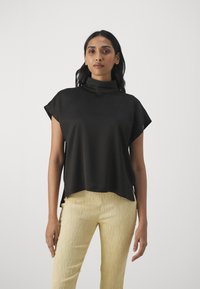Top corto nero con colletto alto, texture liscia e vestibilità ampia, abbinato a pantaloni gialli con texture. Design semplice e moderno.