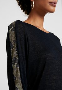 Marineblauer Pullover mit weicher Textur; verfügt über einen gemusterten grünen und schwarzen Akzent entlang des Ärmels, runder Ausschnitt und lockere Passform.