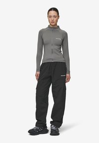 Šviesiai pilkas, ilgas rankovėmis užtrauktuku užsegamas marškinėlis, kuris tiko prie kūno; derinamas su laisvomis juodomis krovinių kelnėmis su kišenėmis, dėvimos su juodais sportbačiais.