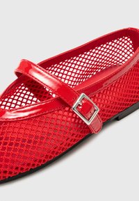 Ballerines en maille rouge avec une sangle en vernis brillant et un détail de boucle, présentant un bout arrondi et une semelle plate en caoutchouc.