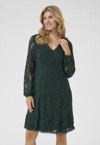 Rochie verde din dantela, cu maneci lungi, transparente, decolteu în V și margine zimțată; prezintă modele florale intricate pe toată suprafața.