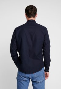 Camisa de botones de manga larga en color marino, con cuello extendido y detalles de botones blancos, hecha de algodón, que presenta una parte posterior recta y un dobladillo redondeado.