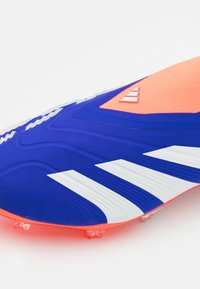 Scarpa da calcio con tomaia blu, strisce bianche, dettagli arancioni, superficie texturizzata e tacchetti trasparenti per una maggiore aderenza.