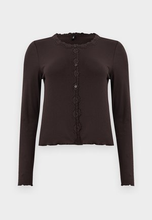 Mørkebrune langermede topp med ribbet tekstur, blonder trim ved utringningen og en knappet front med tre knapper. Bølgete kant.
