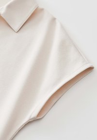 Hellbeige Kurzarm-Poloshirt aus weicher Baumwolle mit klassischem Kragen und gestickten Akzenten entlang der Ärmel und des Saums.