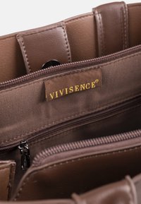 Interior de bolso de cuero marrón que muestra compartimentos con cremallera y una etiqueta de tela con "VIVISENCE" en letras doradas.