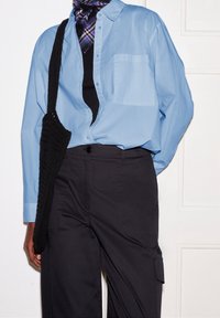 Light blue button-up shirt with long sleeves, black knitted bag, and black cargo pants, featuring a front pocket and textured fabric.