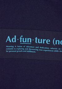 Jūrinės mėlynos medžiagos centre yra vėliava su užrašu "Ad·fun·ture (substantyvas)" šviesiai mėlynai, o žemiau pateikta apibrėžtis tamsiai mėlynos spalvos.