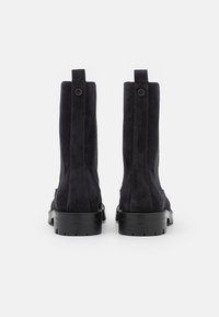Pair of black suede ankle boots with pull tabs and chunky rubber soles, shown from the back on a white background.