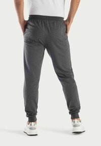 Grijze sweatpants met elastische tailleband, ribgebreide manchetten en zijzakken, gecombineerd met witte sportschoenen. Achteraanzicht, gladde textuur.