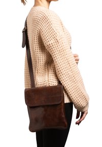 Borsa a tracolla in pelle marrone con chiusura a pattina, texture liscia e tracolla scura regolabile, esposta su uno sfondo chiaro.
