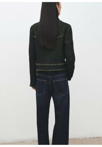Czarny i zielony sweter o fakturze z postrzępionymi krawędziami, zestawiony z ciemnoniebieskimi jeansami o prostych nogawkach, posiadającymi tylne kieszenie i widoczne przeszycia.