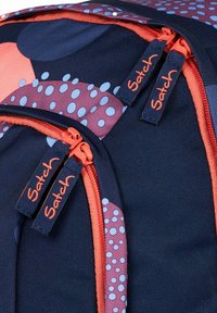Zaino blu navy con accenti a pois color corallo e viola, dotato di quattro cerniere corallo con linguette blu navy etichettate "Satch."