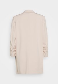 Manteau oversize beige avec un col classique, manches longues et détail froncé aux poignets. Tissu lisse de couleur unie.