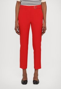 Røde skreddersydde bukser med slim fit, som har belte, glatt tekstur og cropped lengde, sammen med svarte sko. Stripete topp synlig.