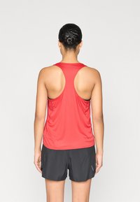 Red racerback tank top made of lightweight fabric, paired with black athletic shorts. Simple design with a smooth texture and no visible patterns.