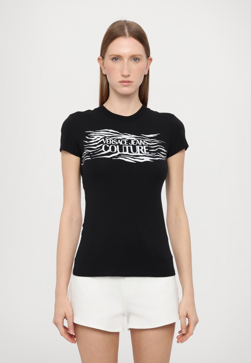Must värviline lühikeste varrukatega t-särk, millel on valge laineline graafiline print, mis ütleb "VERSACE JEANS COUTURE" rinna peal. Peenike disain. Pehme kangas.