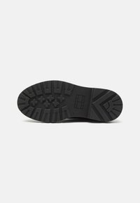 Semelle de chaussure en caoutchouc noir avec un motif de semelle multicouche. Caractéristiques d'un bout arrondi, d'un talon renforcé et d'un logo de marque imprimé sur le côté.
