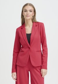 Blazer rouge sur mesure en tissu lisse avec une fermeture à un bouton, des revers crantés et deux poches frontales.