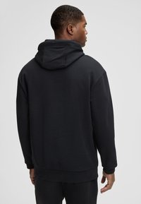 Felpa nera con cappuccio dall'fit rilassato, dotata di cappuccio regolabile, polsini e orlo a coste, realizzata in tessuto morbido e liscio.