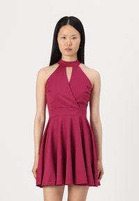 Robe halter bordeaux avec un détail en œillet, corsage ajusté et jupe évasée. Fabriquée en tissu lisse avec une texture douce.