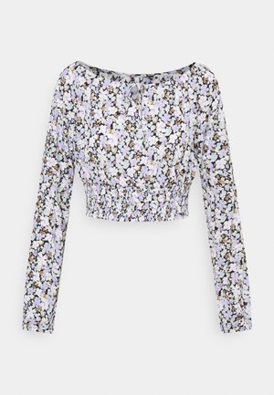 Blouse courte à manches longues avec motif floral lavande, blanc et beige et taille élastiquée sur fond uni.