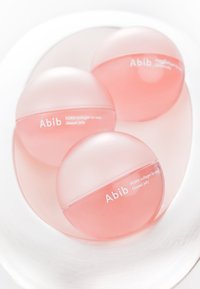 Trois capsules translucides roses portant l'inscription « Abib PDRN collagen lip mask Glazed jelly » reposent sur une surface argentée réfléchissante.