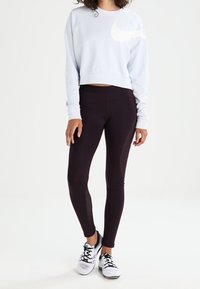 Ljusblå kort sweatshirt med en vit Nike-logotyp, kombinerad med svarta leggings med meshpaneler och vita sportskor.