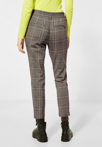 Pantalons à carreaux gris au design ajusté, avec une taille extensible et des poches arrière. Associés à des bottines noires.