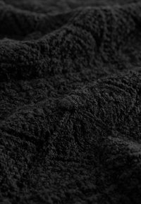 Tessuto nero con una trama profonda, che presenta onde e pieghe. La superficie sembra morbida e leggermente pelosa, con una colorazione scura uniforme.