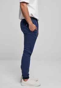 laivyno mėlynos spalvos siauro kirpimo sportinės kelnės iš minkštos medžiagos, su šoninėmis kišenėmis ir briaunotais rankogaliais. Dėvimos su baltais sportbačiais.