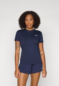 Top atlético azul-marinho com decote redondo e mangas curtas, feito de tecido suave; detalhe do logo no peito. Combinado com calções a condizer.