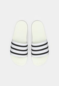 Λευκά σανδάλια τύπου slide με μαύρες και υφασμάτινες λευκές ρίγες στο επάνω μέρος. Λείο υλικό με επίπεδη, εργονομική σόλα. Μινιμαλιστικός σχεδιασμός.