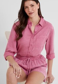 Light pink button-up shirt with long sleeves rolled at the cuffs, paired with matching elastic waistband shorts. Smooth texture, casual design.