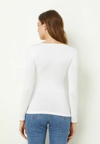 Weißes Langarmhemd mit Rundhalsausschnitt, aus glattem Stoff, kombiniert mit blauen hoch sitzenden Jeans, die eine taillierte Silhouette zeigen.