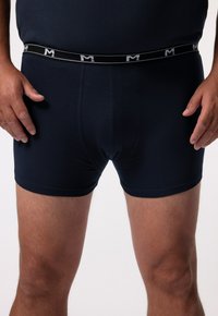 Shorts de boxe bleu marine en tissu doux, dotés d'une taille élastique avec un logo blanc. Style ajusté avec une texture lisse et sans motifs visibles.