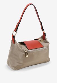 Bolso de nylon beige con una solapa de cuero rojo, herrajes dorados y un bolsillo externo con cremallera. Cuenta con un asa única con un borde negro.