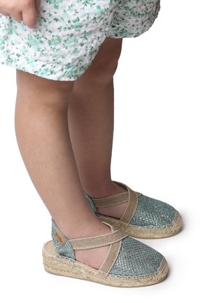 Ljusblå espadriller med elastiska remmar, sula omgiven av jute och en texturerad ovandel, tillsammans med en blommönstrad kjol.