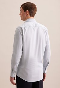 Camicia a maniche lunghe azzurro chiaro con una texture morbida, orlo curvo e polsini bottonati. Presenta un colletto classico e una vestibilità sagomata.