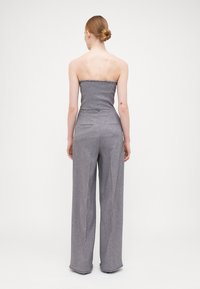 Grå uten ermer jumpsuit med vide bukser. Teksturert stoff med frynset kantdetaljer. Skreddersydd passform fremhever silhuetten.