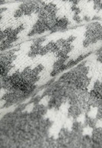 Grau-weißer, gemusterter Strickstoff mit einer weichen, flauschigen Textur, der ein geometrisches Design aufweist, das Sterne oder Schneeflocken ähnelt.