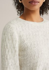 Pulover verde deschis tricotat cu model în formă de diamant, realizat dintr-un material moale și pufos. Are un decolteu rotund și manșete ribbed.