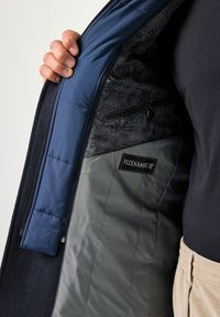 Granatowy płaszcz z ociepleniem, z podszewką w kwiatowy wzór, szarą warstwą zewnętrzną i widoczną metką "FLEXNAMIC IP" w pobliżu kieszeni.