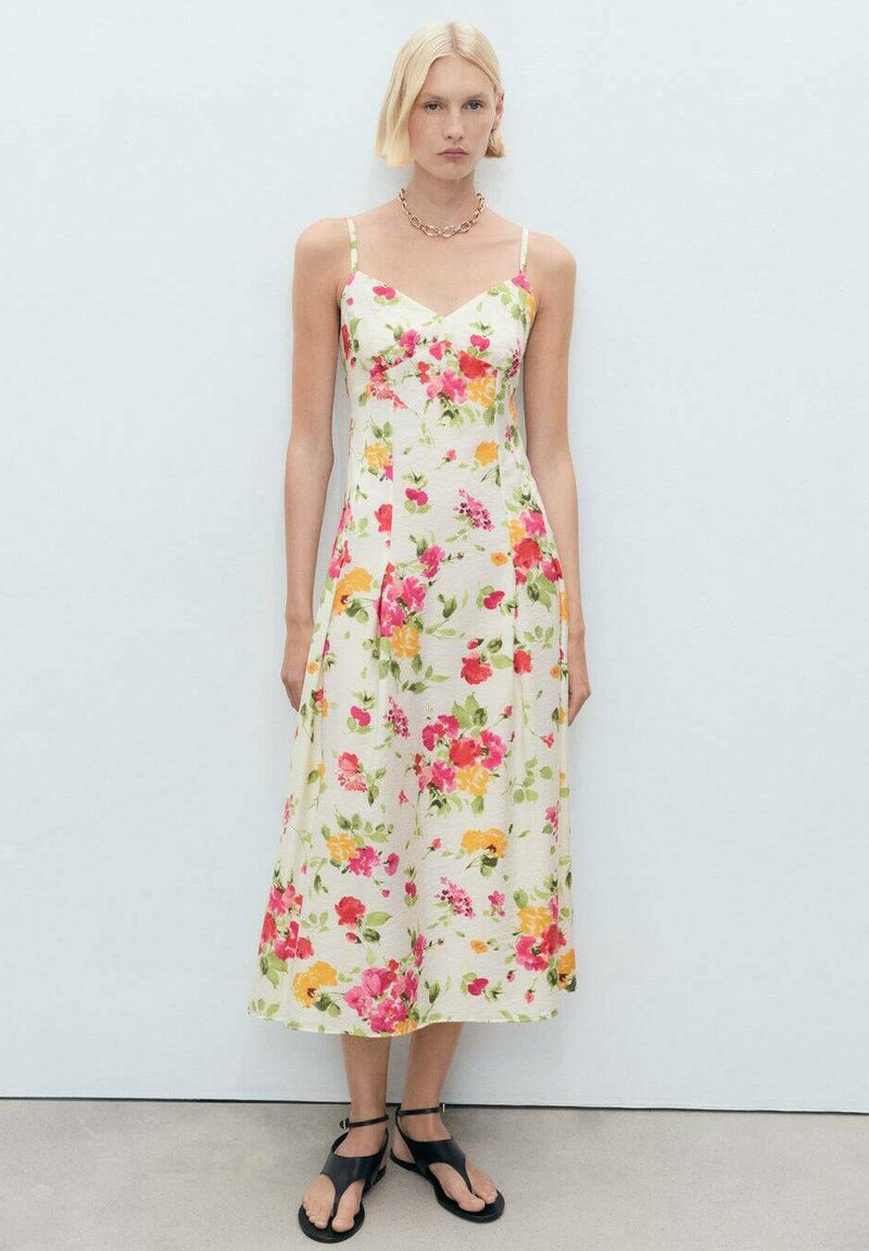 Robe midi florale en tissu crème avec des motifs roses, orange et verts. Présente des bretelles fines et un corsage ajusté, avec une jupe évasée.