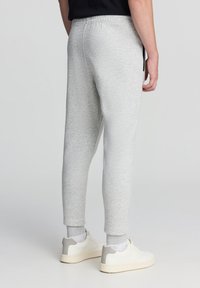 Jasnoszare spodnie dresowe z elastycznym pasem, zwężanymi nogawkami oraz bocznymi kieszeniami, zestawione z białymi sneakersami z szarymi akcentami.