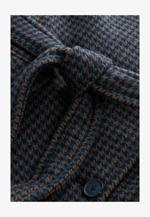 Cappotto in misto lana con un motivo houndstooth blu scuro e marrone, caratterizzato da una vita legata e un dettaglio con bottone nero. Tessuto morbido e strutturato.