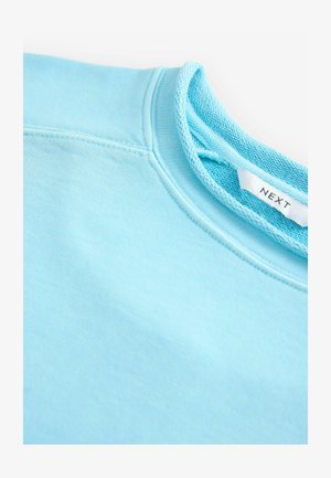 Felpa azzurra chiara con colletto a costine texturizzato. Presenta un'etichetta di marca visibile e un tessuto morbido.