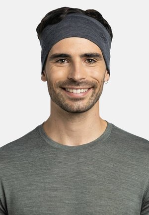 Man with dark hair wearing a gray headband and gray shirt, smiling, against a plain light background.